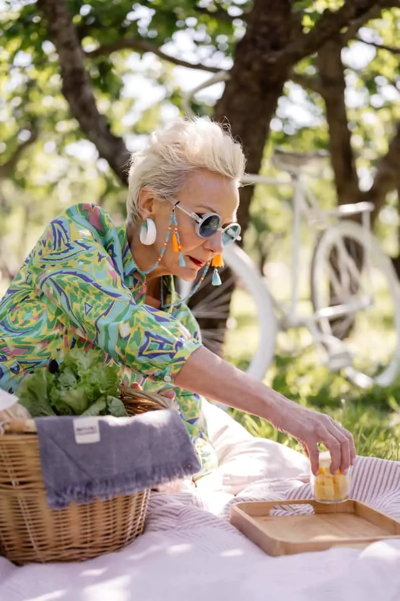 Senior woman in sunglasses at a colorful summer picnic outdoors, surrounded by nature and greenery.